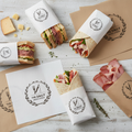 Custom printed deli wrapping paper flat lay with wrapped sandwiches on wooden surface